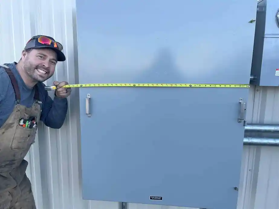 A 509 Electric crew member smiling with a tape measure across a new electrical enclosure